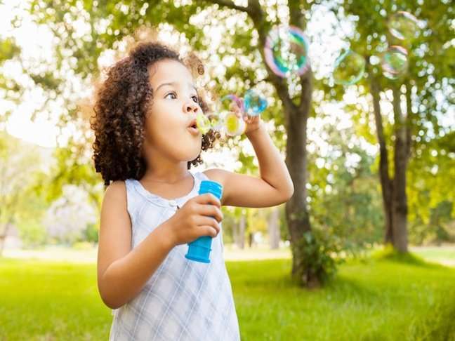 Beautiful little girl blowing bubbles in park. Horizontal Shot.