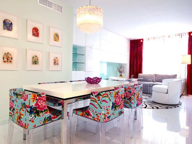 Dining room area with chandelier, bright colorful pink and blue chairs, large mirror on wall, and framed art panels on other wall.