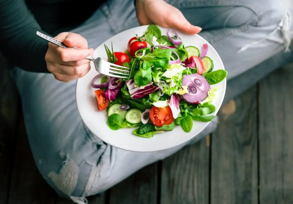 a-person-sitting-on-the-floor-eating-a-healthy-salad.webp