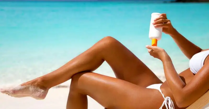 Woman-in-bikini-applying-sunscreen-lotion-at-a-tropical-beach.webp